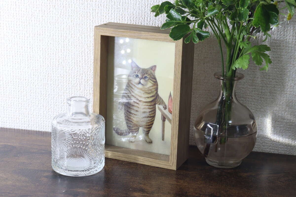 猫の写真立ての横に2種類の花瓶と緑の植物が飾られている棚の上