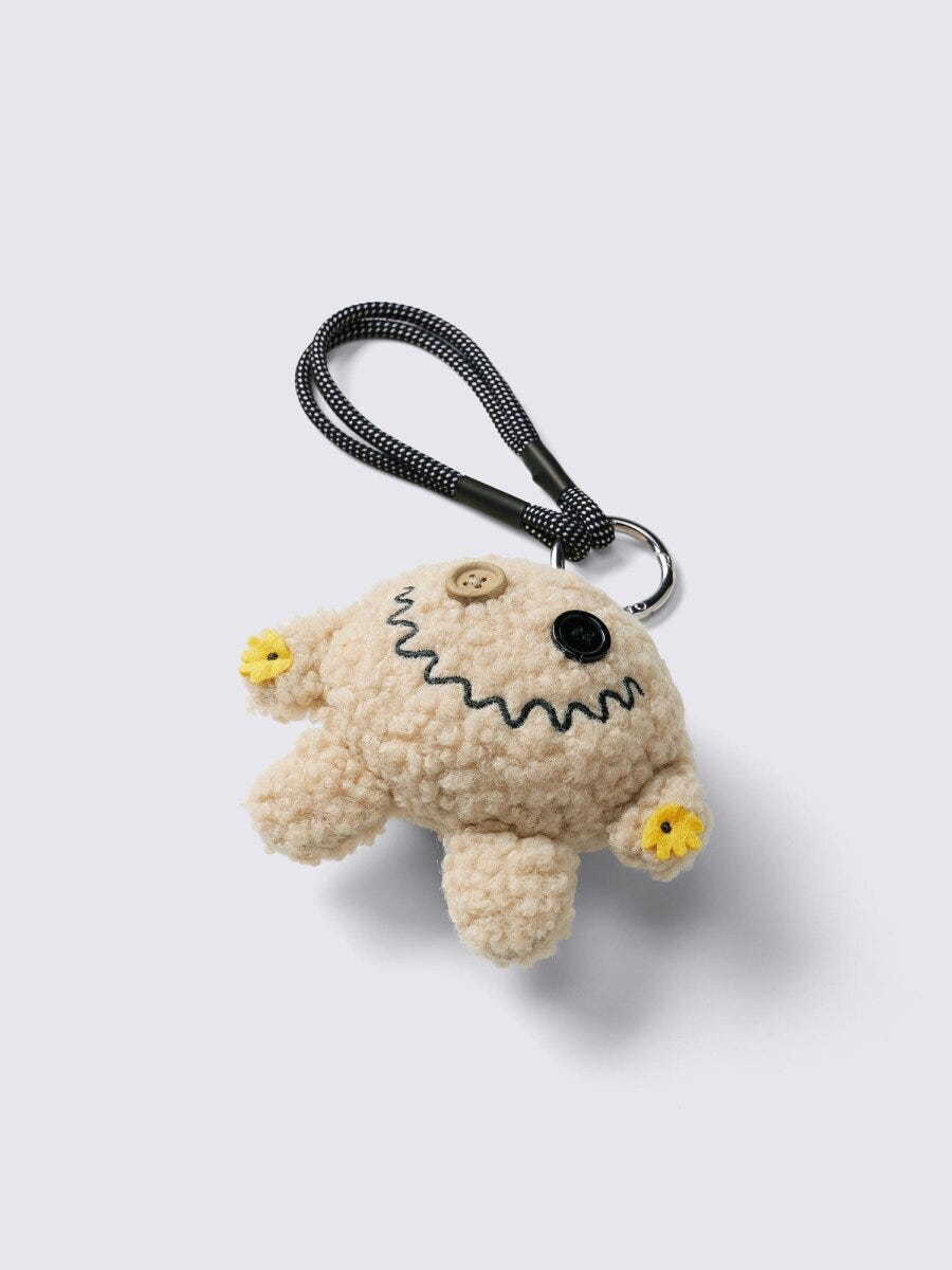 ベージュのふわふわしたモンスター型チャーム。ボタンの目と口が特徴 ベージュのふわふわしたモンスター型チャーム。ボタンの目と口が特徴