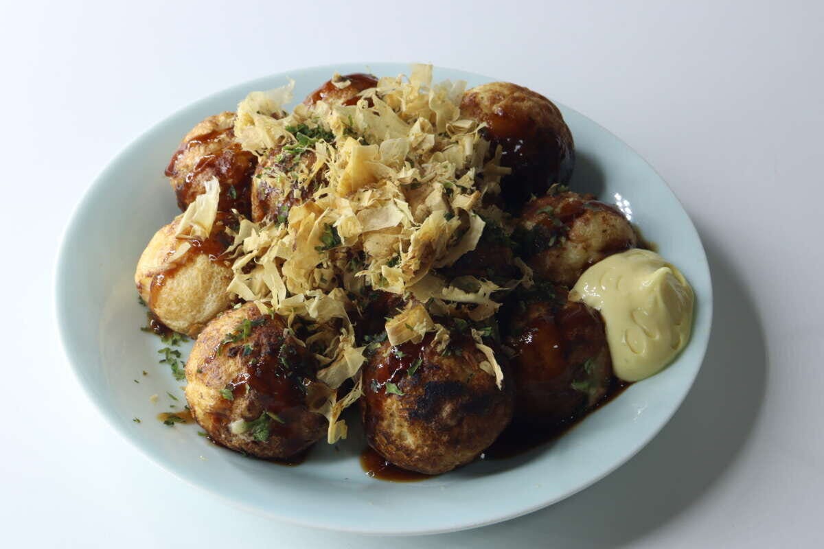 青い皿に盛り付けられたたこ焼きにソース、マヨネーズ、鰹節、青のりがかかっている