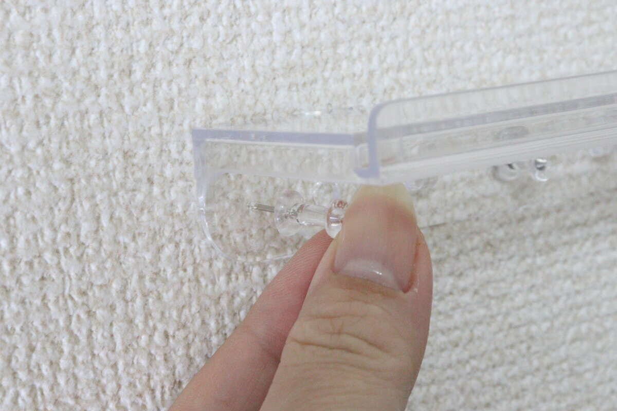 クリアスタンドをプッシュピンで壁に取り付けている手元 クリアスタンドをプッシュピンで壁に取り付けている手元