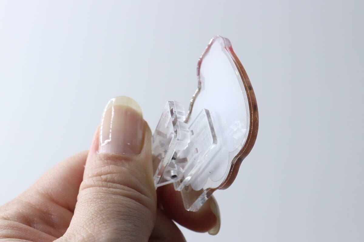 指で持たれた、求心フレンズのアクリルメモスタンド裏面。透明なクリップが見える。