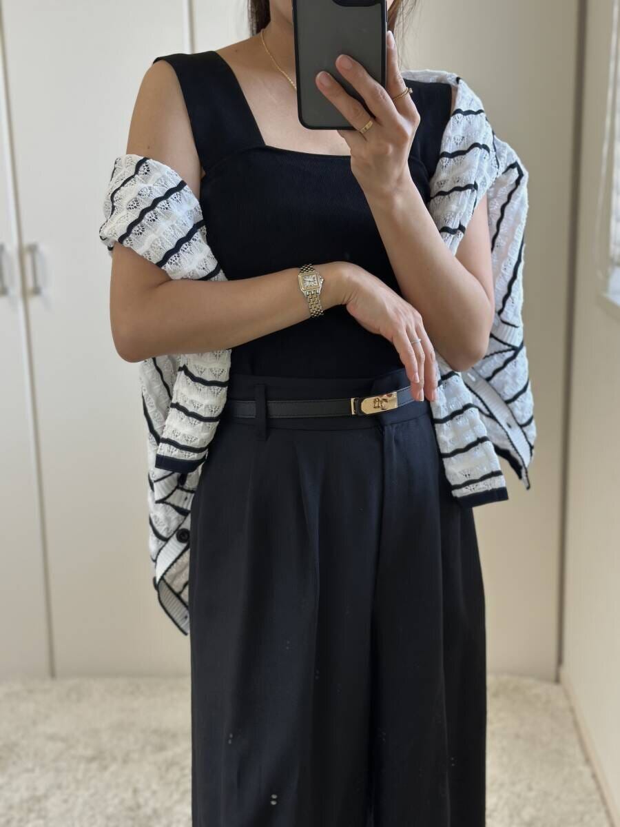 黒いニットインナーとワイドパンツにボーダーカーディガンを肩掛けしスマホを持つ女性 黒いニットインナーとワイドパンツにボーダーカーディガンを肩掛けしスマホを持つ女性