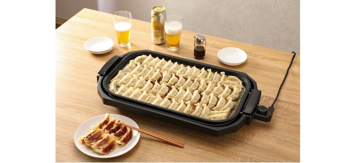 ホットプレートでたくさんの餃子が焼かれ、手前には焼き餃子とビール
