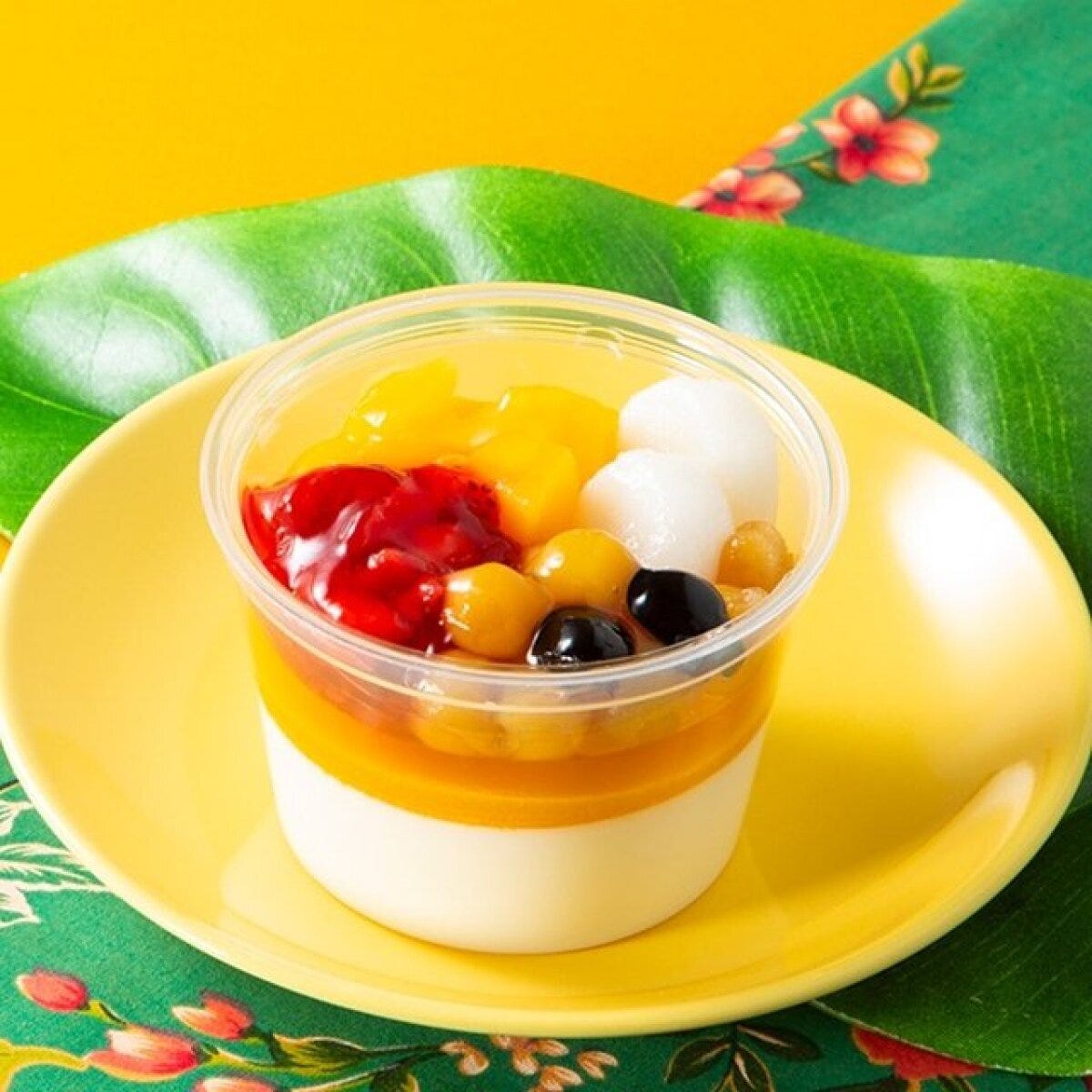 黄色い皿に乗った透明なカップデザート。マンゴーやいちご、豆などカラフルな具材が盛り付けられている。