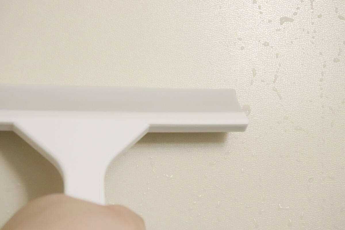 白い水切りワイパーを使って、水滴がついた浴室の壁を水切りしている様子 白い水切りワイパーを使って、水滴がついた浴室の壁を水切りしている様子