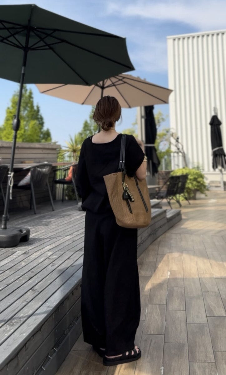 黒いリネンセットアップの女性が屋外テラスで後ろ向きに立つ 黒いリネンセットアップの女性が屋外テラスで後ろ向きに立つ