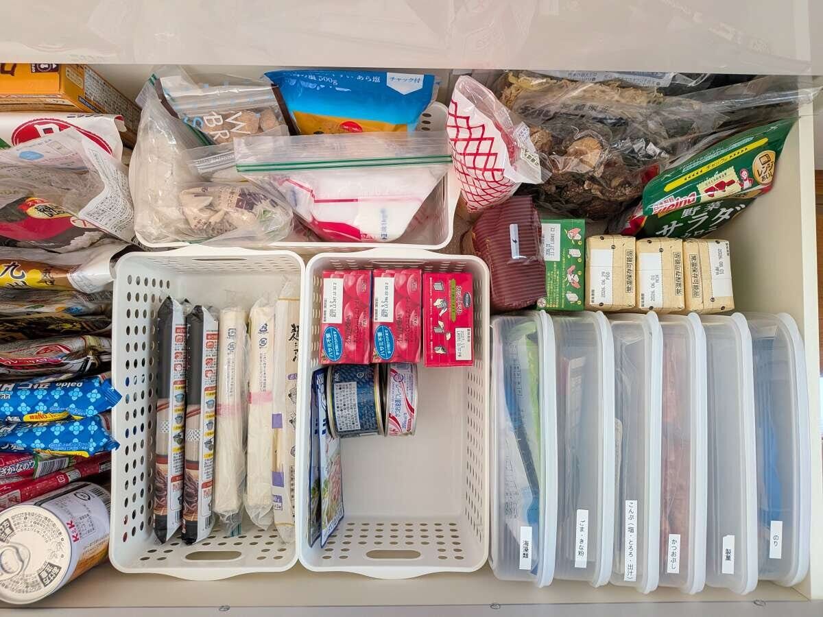 食品ストックを立てて整理した引き出し収納の俯瞰 キッチンの引き出しを真上から見た俯瞰写真。白い収納ボックスに乾麺・缶詰・お菓子の箱を立てて収納し、右側にはラベルを貼ったクリアケースが並んでいる