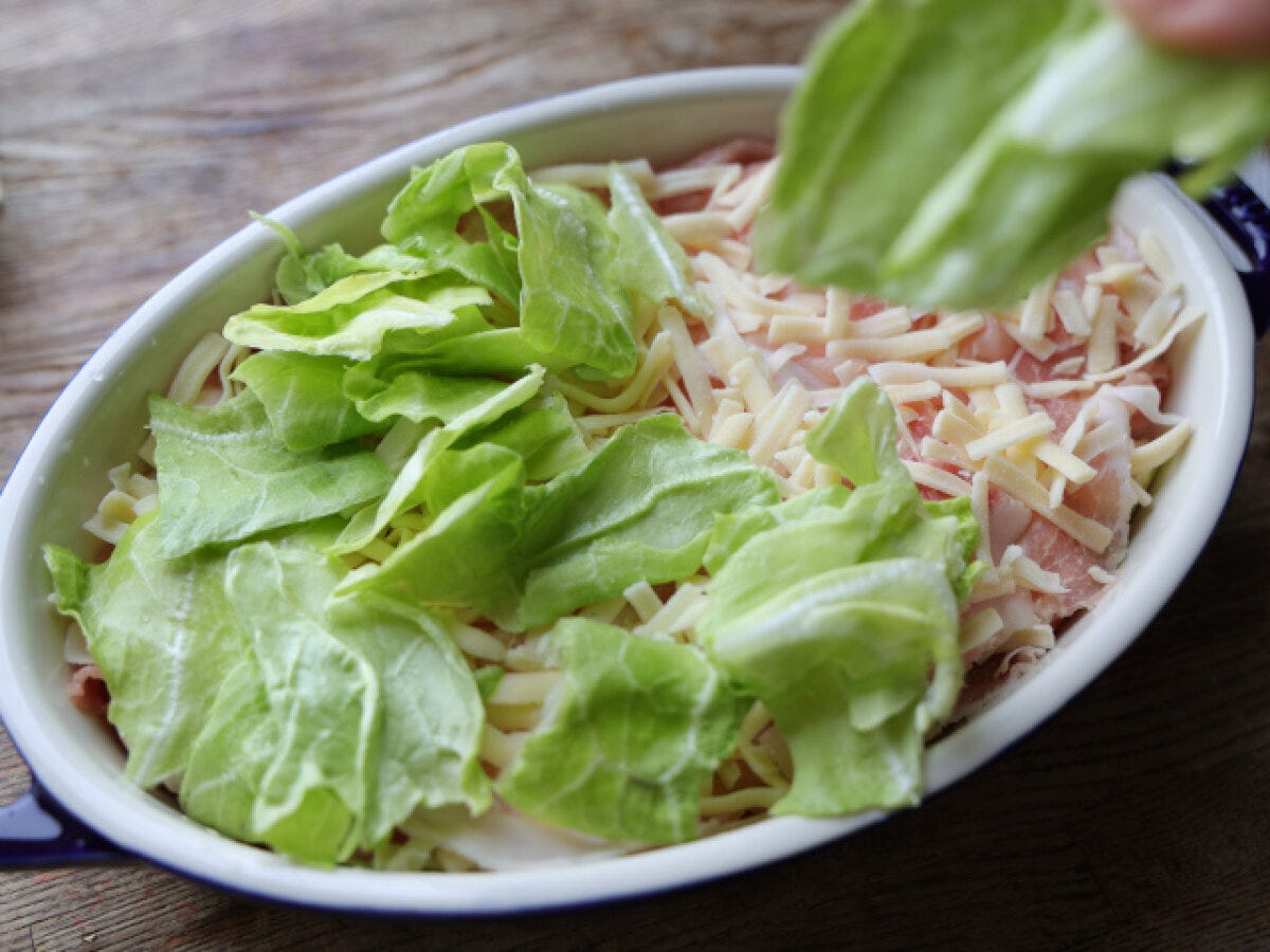 豚肉とチーズの上に、ちぎった春キャベツを手で重ねていく様子