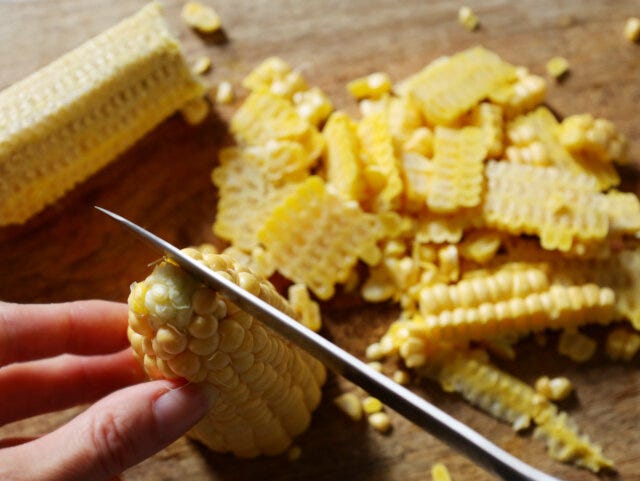 とうもろこしは、皮を剥いて半分にしたら、実を包丁でこそげ取る。