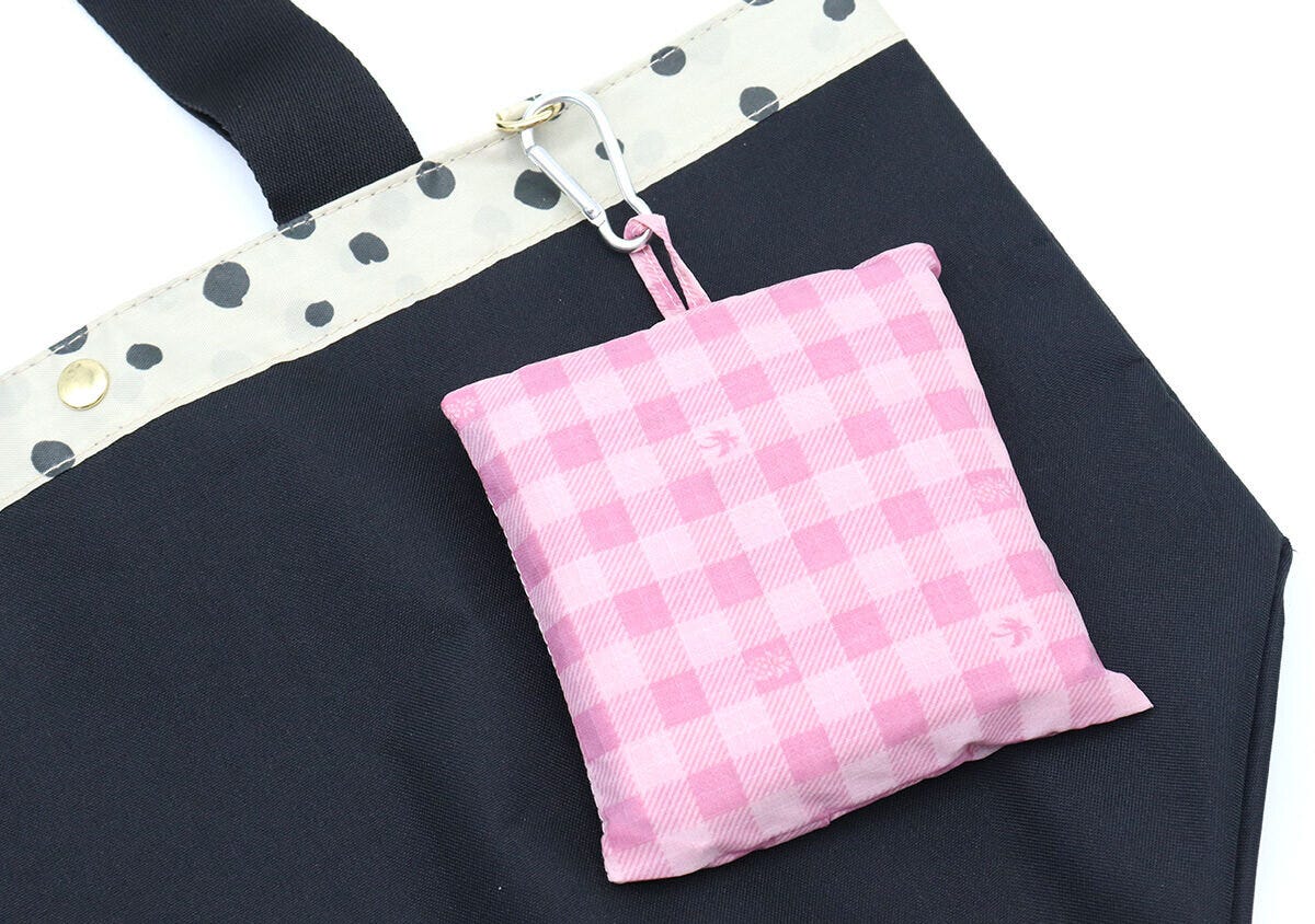 ピンクのチェック柄の折りたたみポーチをカラビナで黒いトートバッグの外側に取り付けた写真
