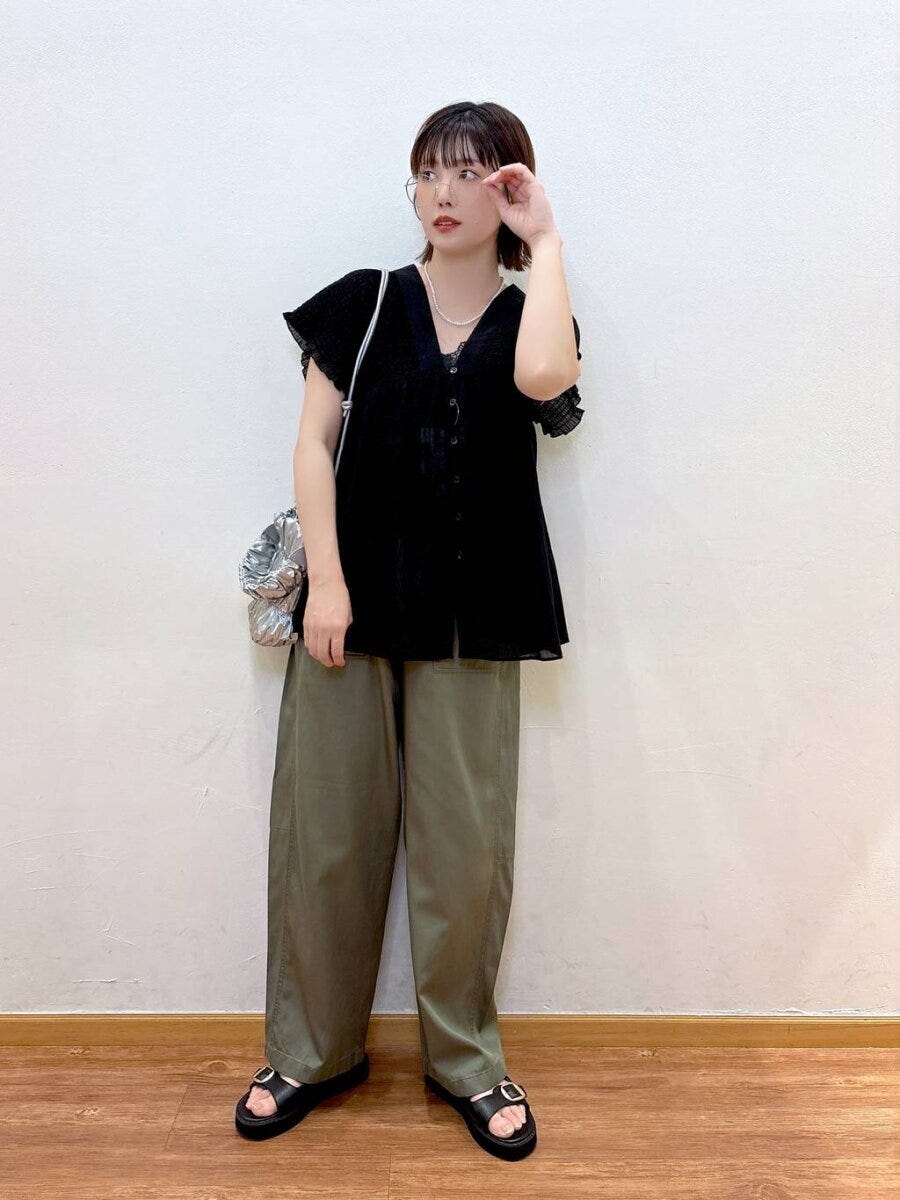 黒のギャザーブラウスとカーキワイドパンツを着てメガネに手を添える女性 黒のギャザーブラウスとカーキワイドパンツを着てメガネに手を添える女性