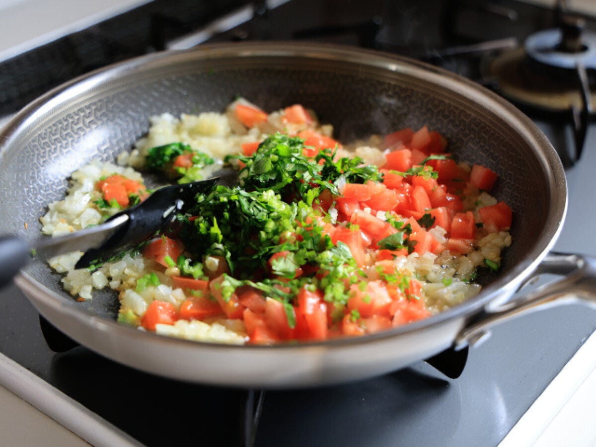 フライパンの炒めた玉ねぎに角切りトマトとみじん切りパクチーを加えた様子