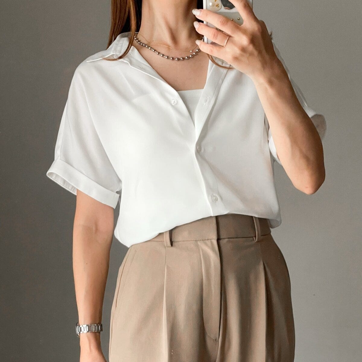 白い半袖シャツとベージュパンツの女性がスマホで自撮りしている 白い半袖シャツとベージュパンツの女性がスマホで自撮りしている