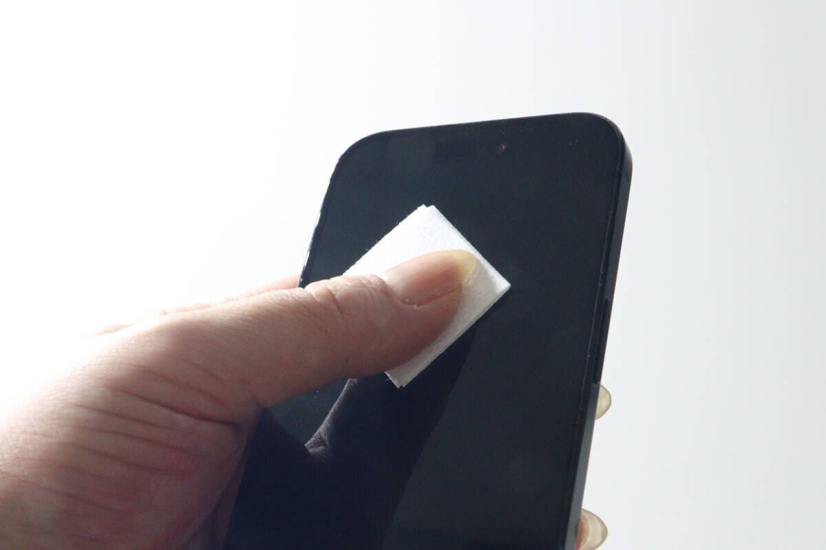 女性の手がスマホ画面の側面をウェットシートで拭いている様子 女性の手がスマホ画面の側面をウェットシートで拭いている様子
