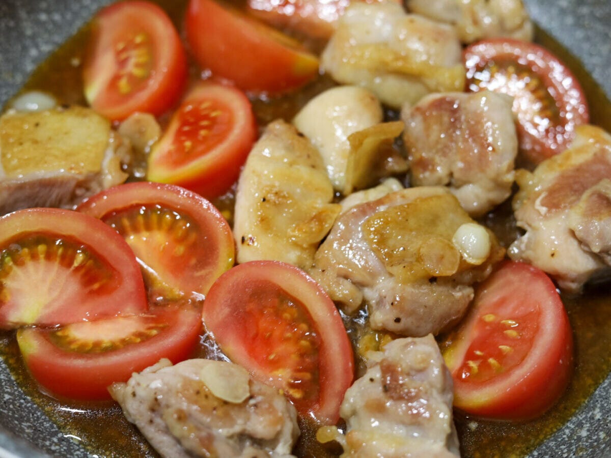 鶏もも肉にトマトと調味料を加える工程 焼いた鶏もも肉にくし切りトマトと合わせ調味料を加えて炒め合わせている様子