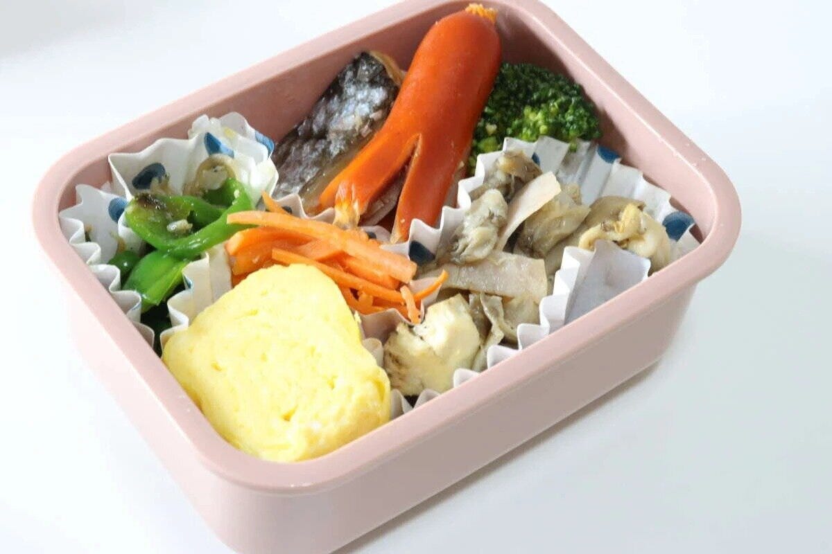 ピンク色の弁当箱の下段に、卵焼き、ウインナー、野菜などのおかずが詰められている ピンク色の弁当箱の下段に、卵焼き、ウインナー、野菜などのおかずが詰められている