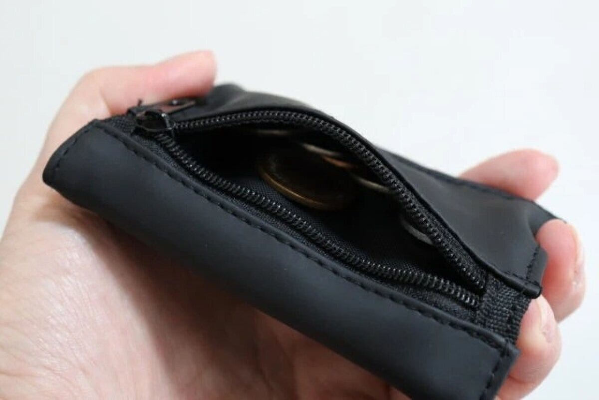 黒い三つ折り財布のファスナー付き小銭入れに小銭が入っている 黒い三つ折り財布のファスナー付き小銭入れに小銭が入っている