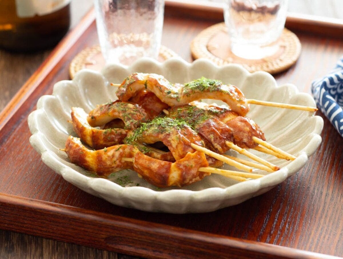 マヨソースで炒めたちくわを串に刺し青のりをかけた料理が花形の白い皿に盛られている