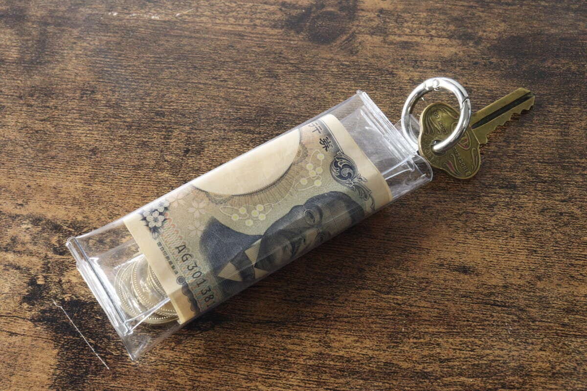 PVCコインポーチに硬貨と千円札、鍵がリングに取り付けられて木目のテーブルに置かれている