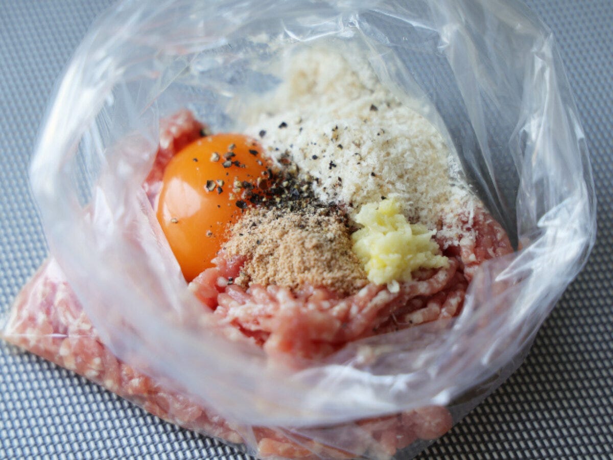 ビニール袋で肉だねの材料を混ぜる工程 ビニール袋にひき肉・卵・パン粉・すりおろしにんにく・黒こしょうを入れた肉だねの材料のアップ俯瞰写真