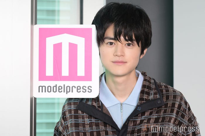 モデルプレスのロゴを壁と挟み遊んでいた鈴鹿央士さん(C)モデルプレス