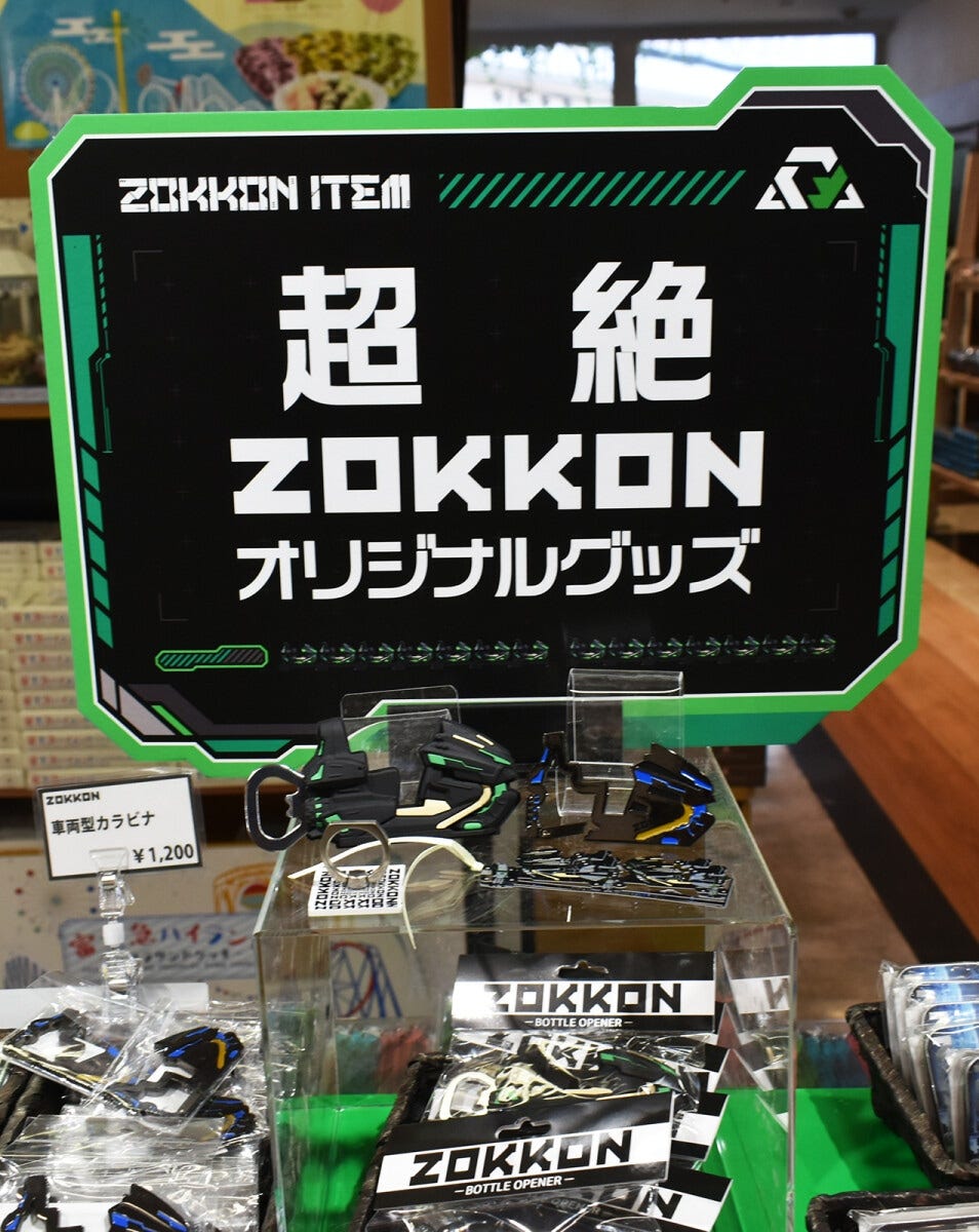 “超絶ZOKKONオリジナルグッズ”の看板の下にあるのは、ZOKKONマグネット栓抜き 1250円、ZOKKON車両型カラビナ 1200円、ZOKKONブックマーカー 1200円、ZOKKONスマホリング 1200円
