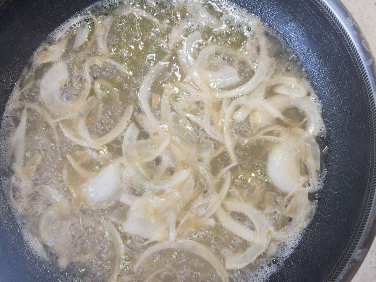 フライパンで薄切り玉ねぎとみじん切りにんにくがバターで炒められている様子