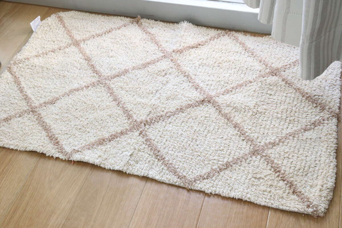 窓際に敷かれたベージュのダイヤ柄フロアマットと白いカーテン