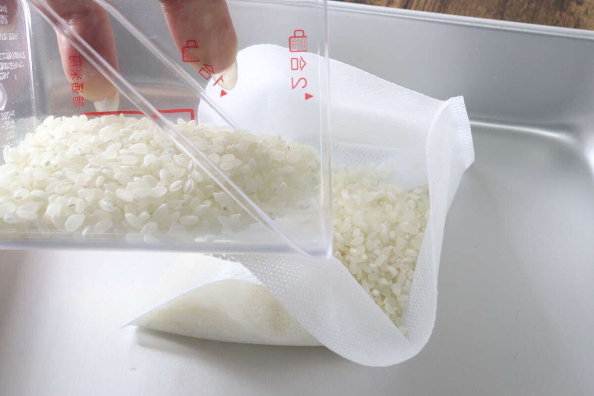 計量カップから白い生米を不織布の炊飯袋へ入れている工程
