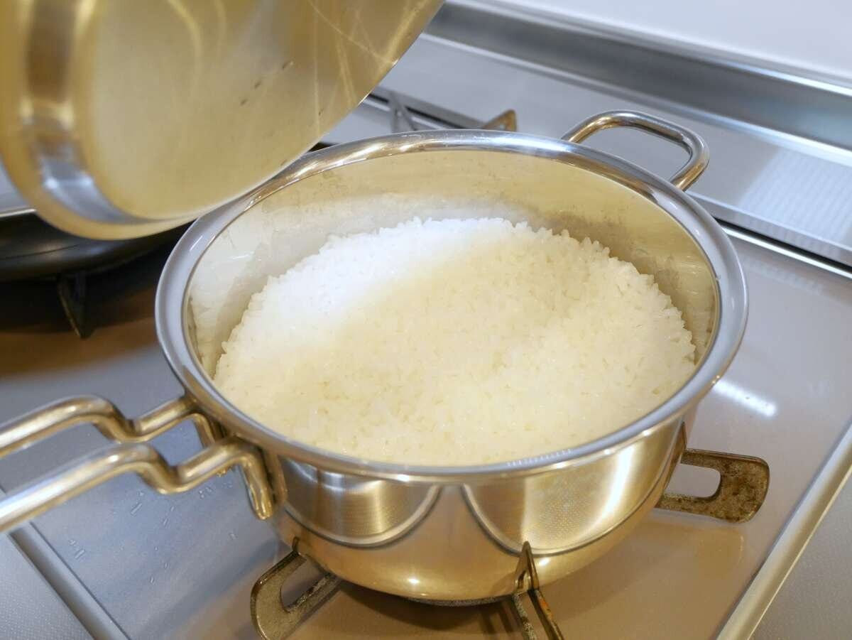 ガスコンロの上でステンレス鍋のふたを開けて炊き上がった白ご飯が見える鍋炊飯の様子 ガスコンロの上でステンレス鍋のふたを開けて炊き上がった白ご飯が見える鍋炊飯の様子