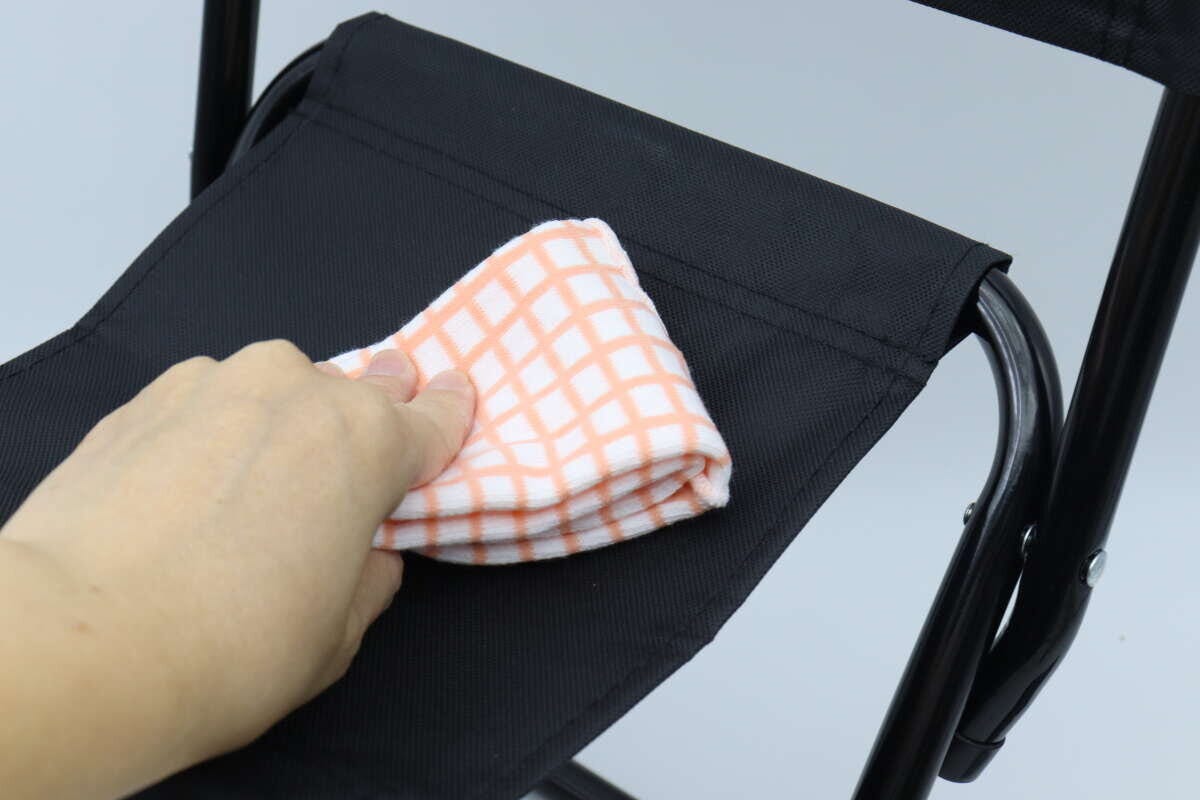 手がレジャー椅子の座面をチェック柄の布で拭いている