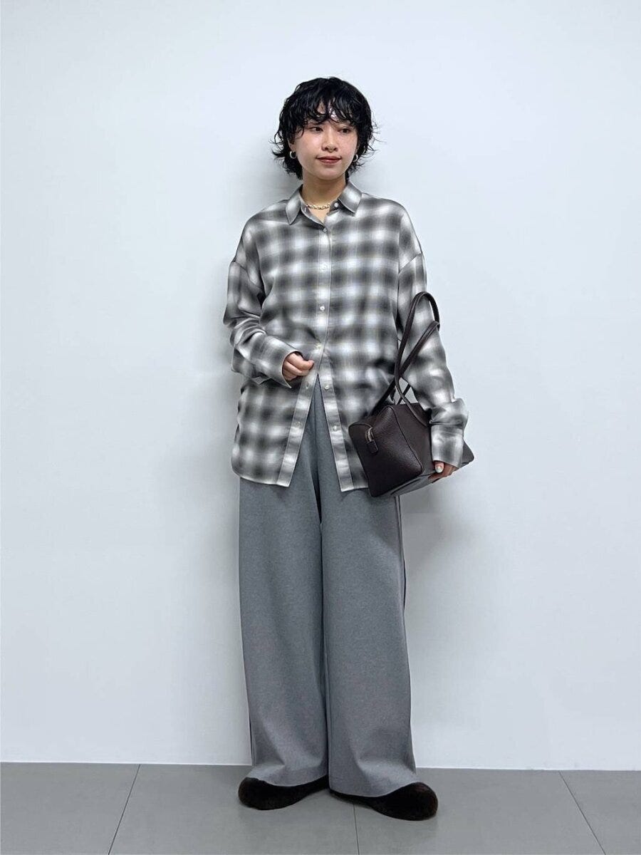 グレーのチェック柄シャツとスウェットパンツを着て黒いバッグを持つ女性