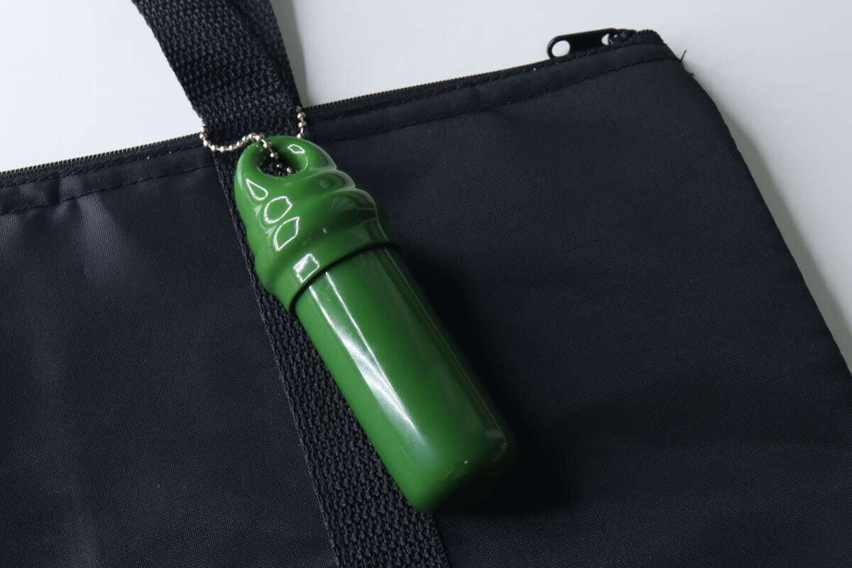 緑色の小物入れキーホルダーが黒いバッグの持ち手にボールチェーンで取り付けられている