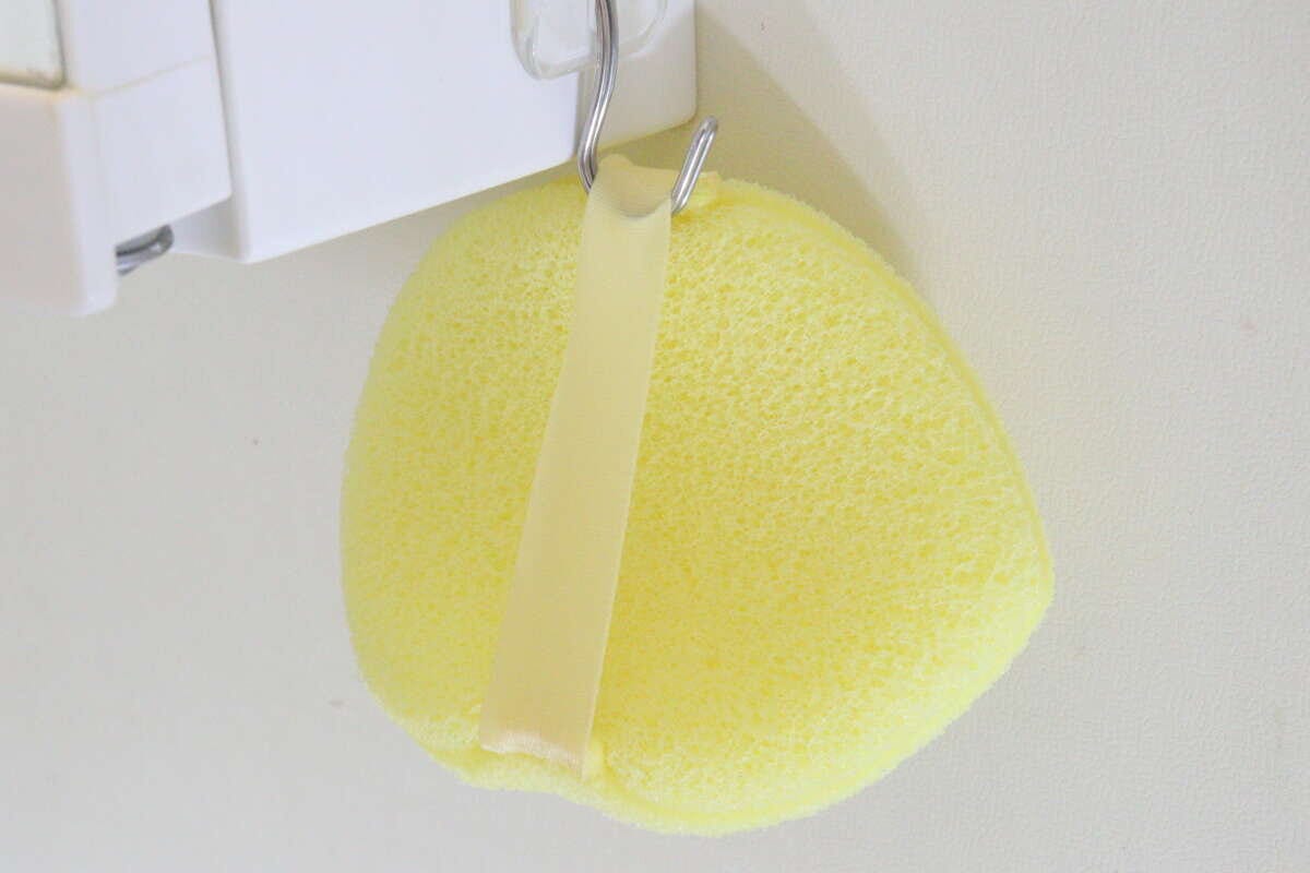 黄色い洗顔パフのベルト部分をフックに掛けて乾燥させている