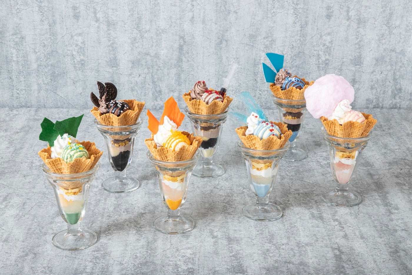 （最奥左から）死柄木弔の敵（ヴィラン）パフェ／トガヒミコの敵（ヴィラン）パフェ／荼毘の敵（ヴィラン）パフェ<br>
（手前左から）緑谷出久のヒーローパフェ／爆豪勝己のヒーローパフェ／轟焦凍のヒーローパフェ／麗日お茶子のヒーローパフェ各1,490円（税込）（C）堀越耕平／集英社