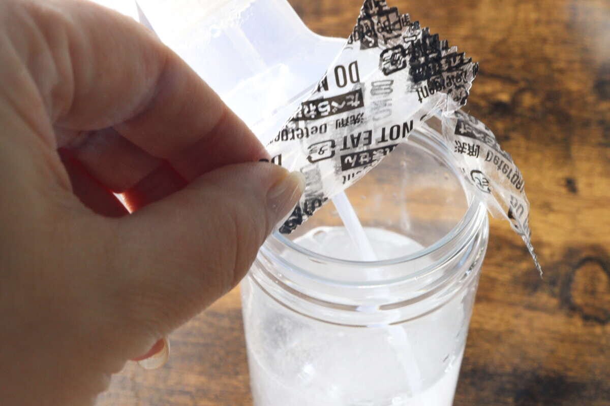 手で個包装から取り出した錠剤型クリーナーを水が入った容器に入れている