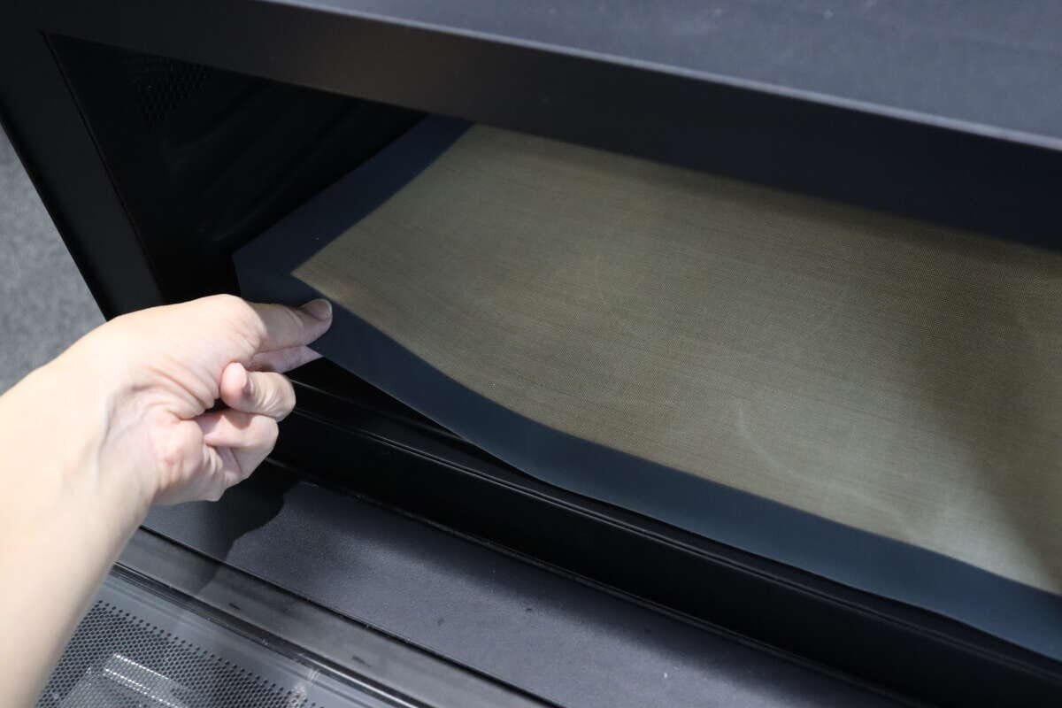 電子レンジの庫内にベージュ色のマットを敷き入れている手元