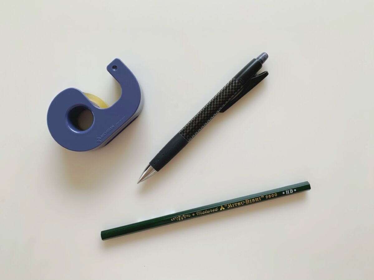 白い机の上に置かれたテープカッターとシャープペンシルと鉛筆