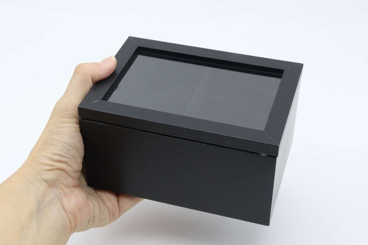 黒い腕時計用収納BOXを片手で持ち上げている