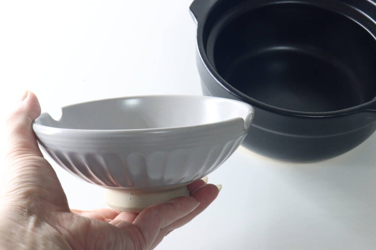 女性の手が、茶碗として使えるグレーの土鍋の蓋を持っている 女性の手が、茶碗として使えるグレーの土鍋の蓋を持っている