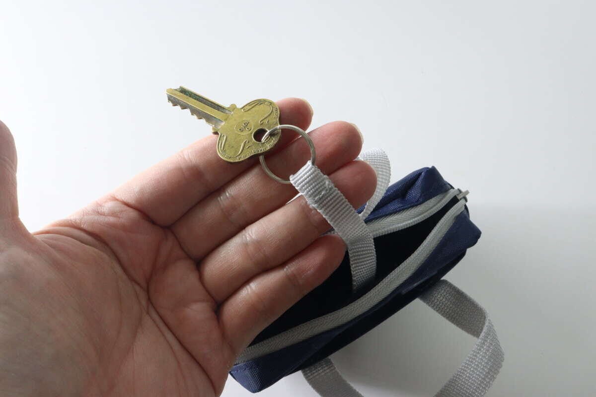 手がポーチのキーリングに鍵を取り付けている様子 手がポーチのキーリングに鍵を取り付けている様子