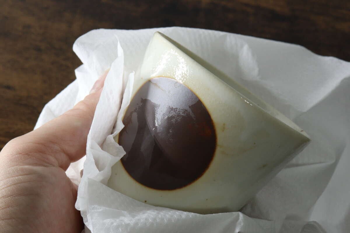 キッチンペーパーで茶色の模様がある器を拭いている手