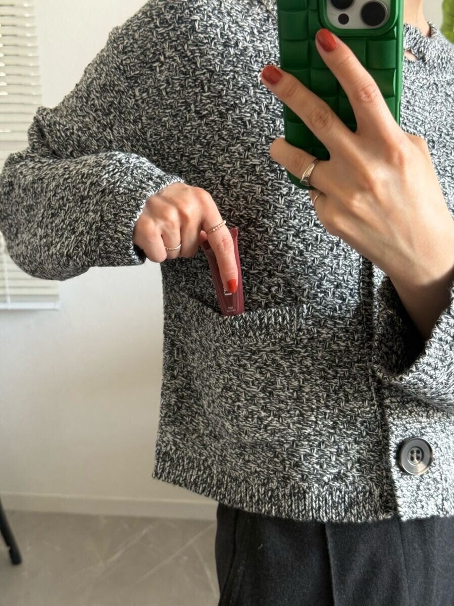 女性がツイード風カーディガンのポケットにリップを入れる 女性がツイード風カーディガンのポケットにリップを入れる