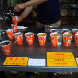 大きなタンクから温かい涼茶がカップに並々と注がれます。お店の人に10$を手渡して、好みの涼茶を受け取る/提供画像