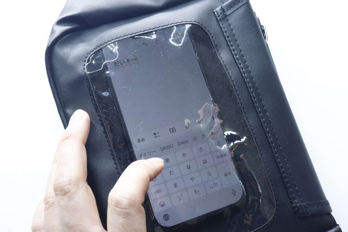 黒いバッグのクリア窓越しにスマートフォンを指で操作している