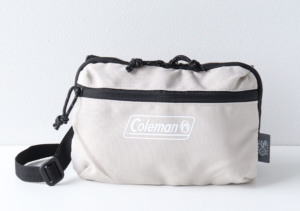 Colemanロゴ入りベージュの長方形ミニショルダーバッグ正面写真。ドローコードとフロントジッパーポケット付き