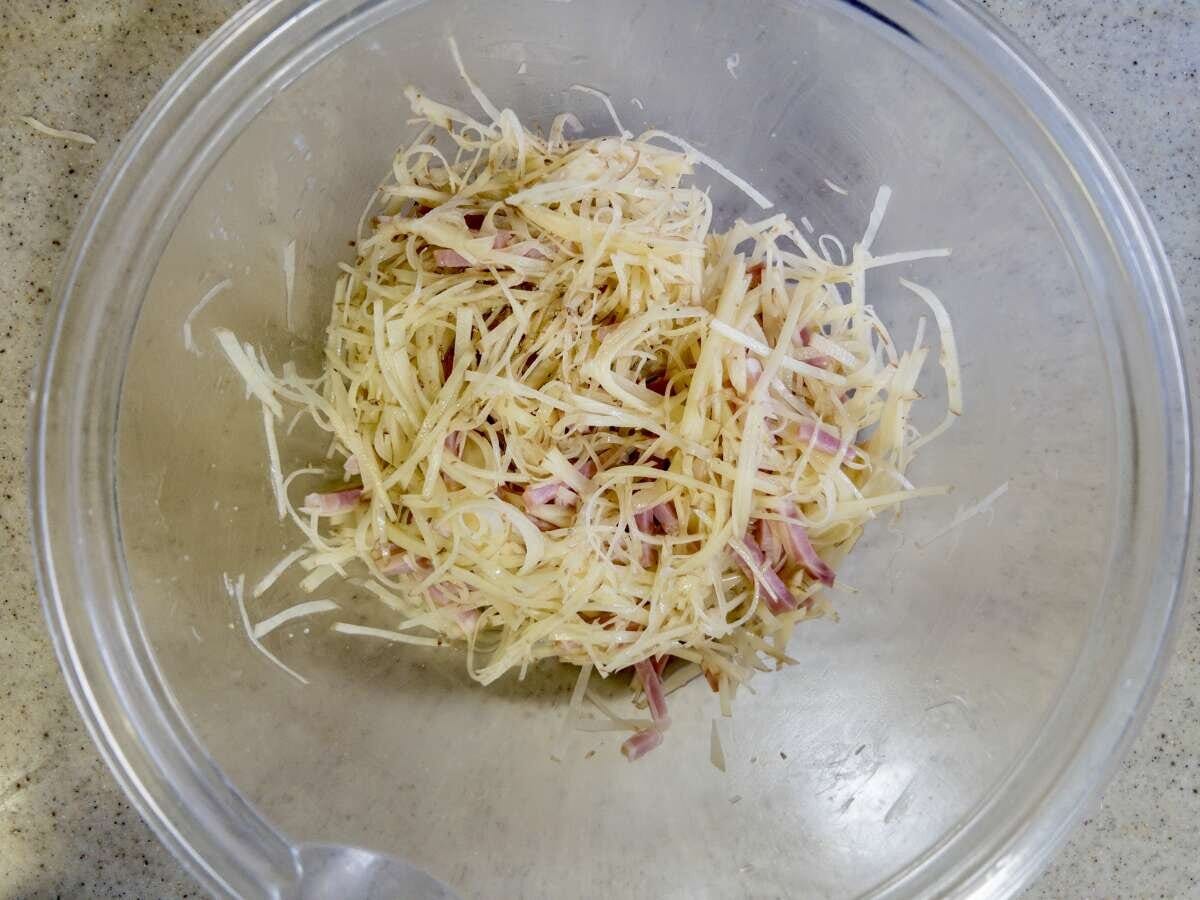 千切りにした新じゃがいもとベーコンをガラスのボウルで混ぜ合わせている様子