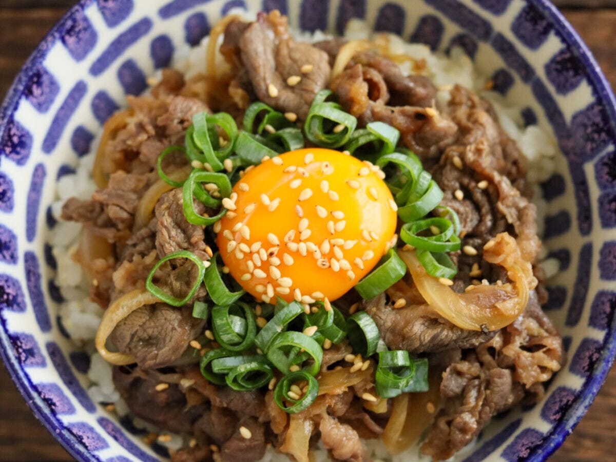 模様の丼にご飯と炒めた牛肉、卵黄、小ねぎ、白いりごまが盛られたスタミナ丼の俯瞰 模様の丼にご飯と炒めた牛肉、卵黄、小ねぎ、白いりごまが盛られたスタミナ丼の俯瞰