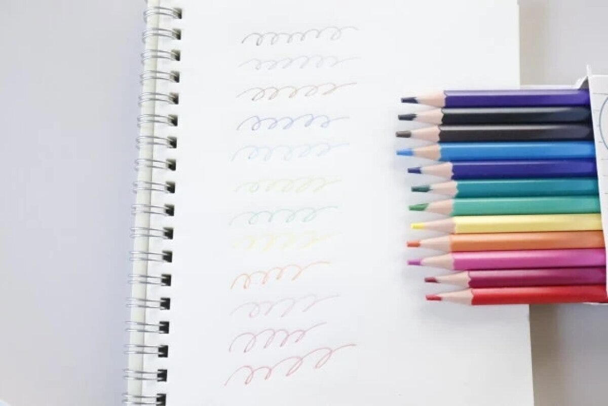 ノートに色鉛筆で波線が描かれ、色鉛筆の箱が横に置かれている ノートに色鉛筆で波線が描かれ、色鉛筆の箱が横に置かれている