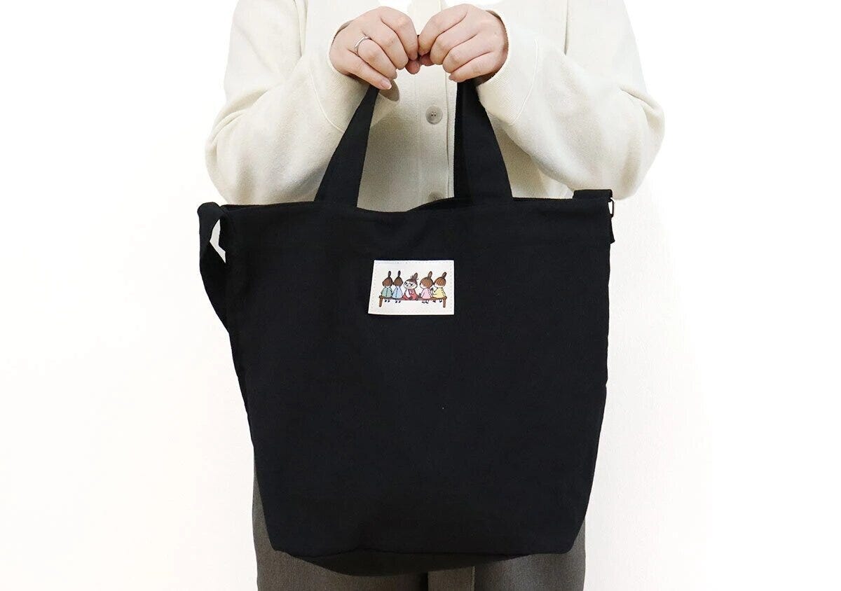 MOOMINのリトルミイ柄ワッペン付き黒ショルダーバッグを手持ちする女性